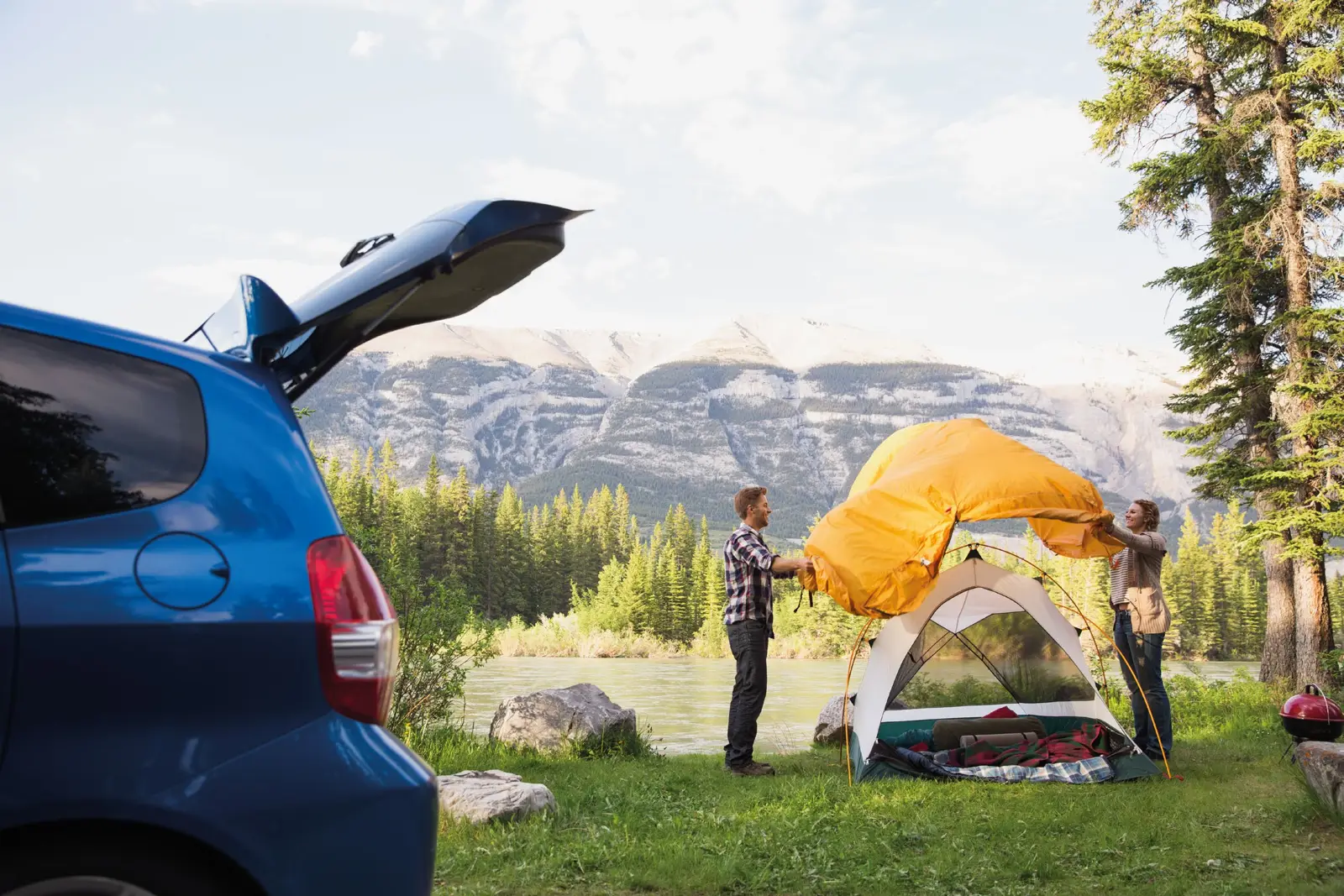 Pareja armando una carpa junto a su auto en un lago de montaña